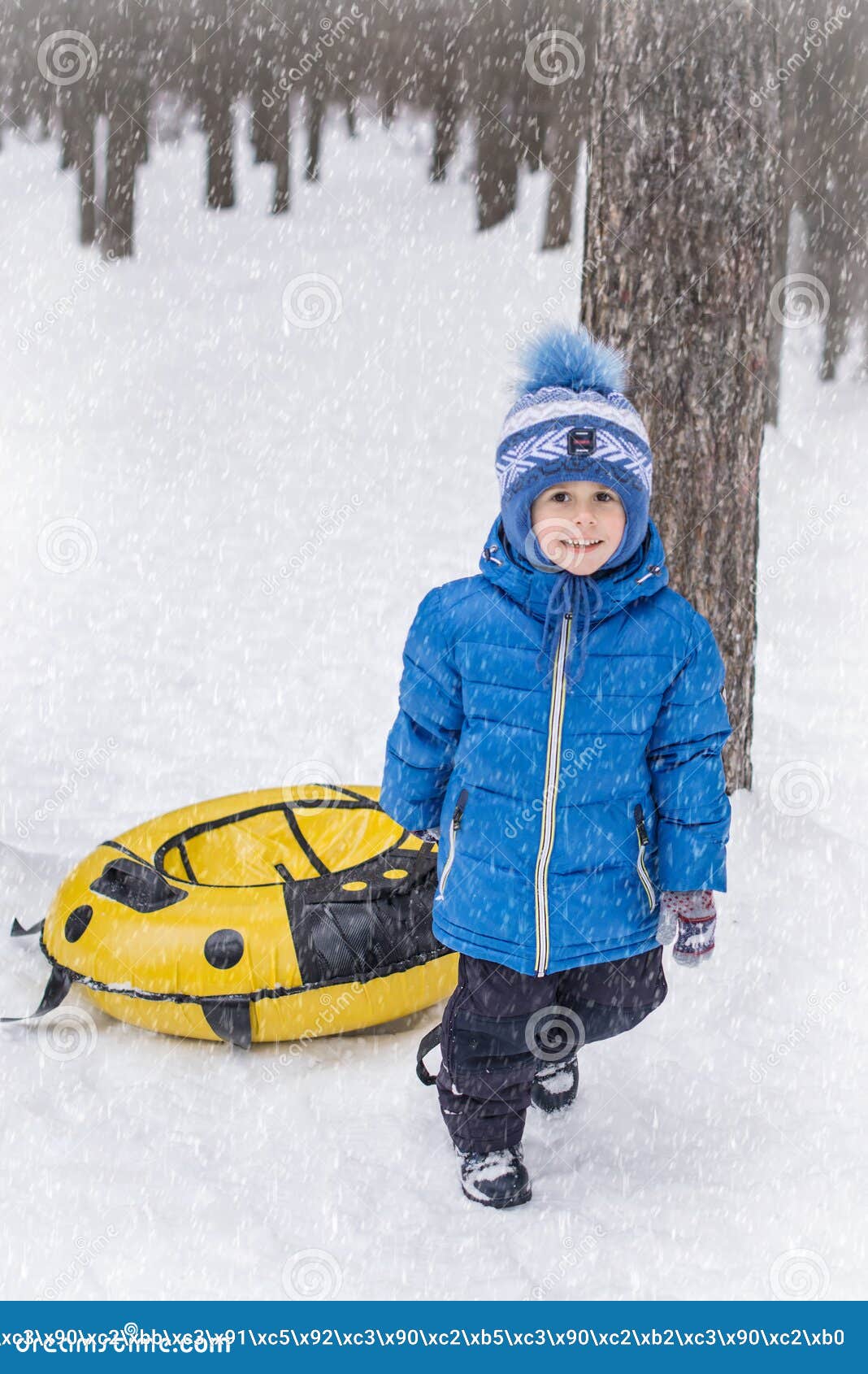 little boy in a blue coat holding yellow inflatable snowtube on winter day