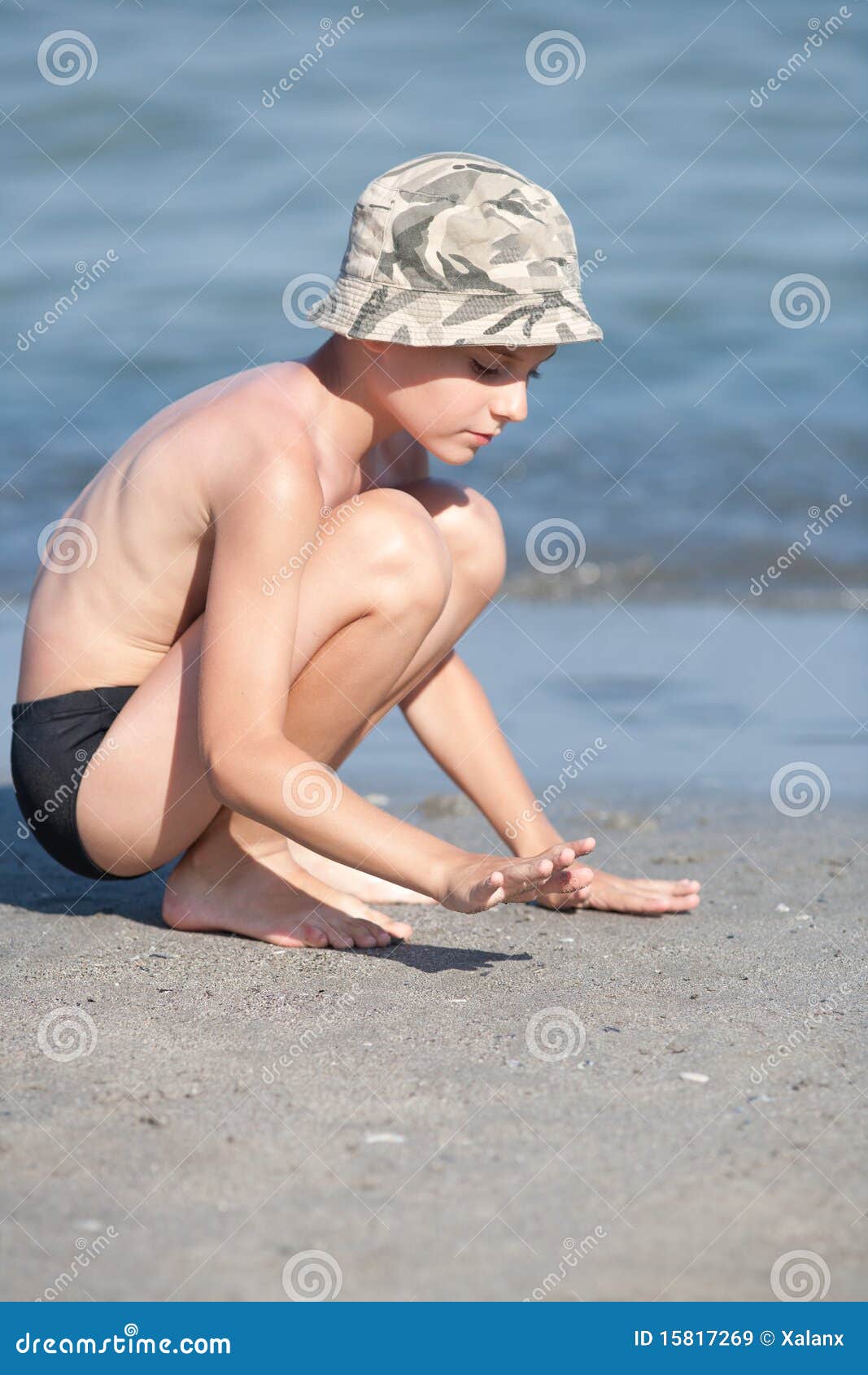 Cute little boy sitting on stone, beach Stock Photo by