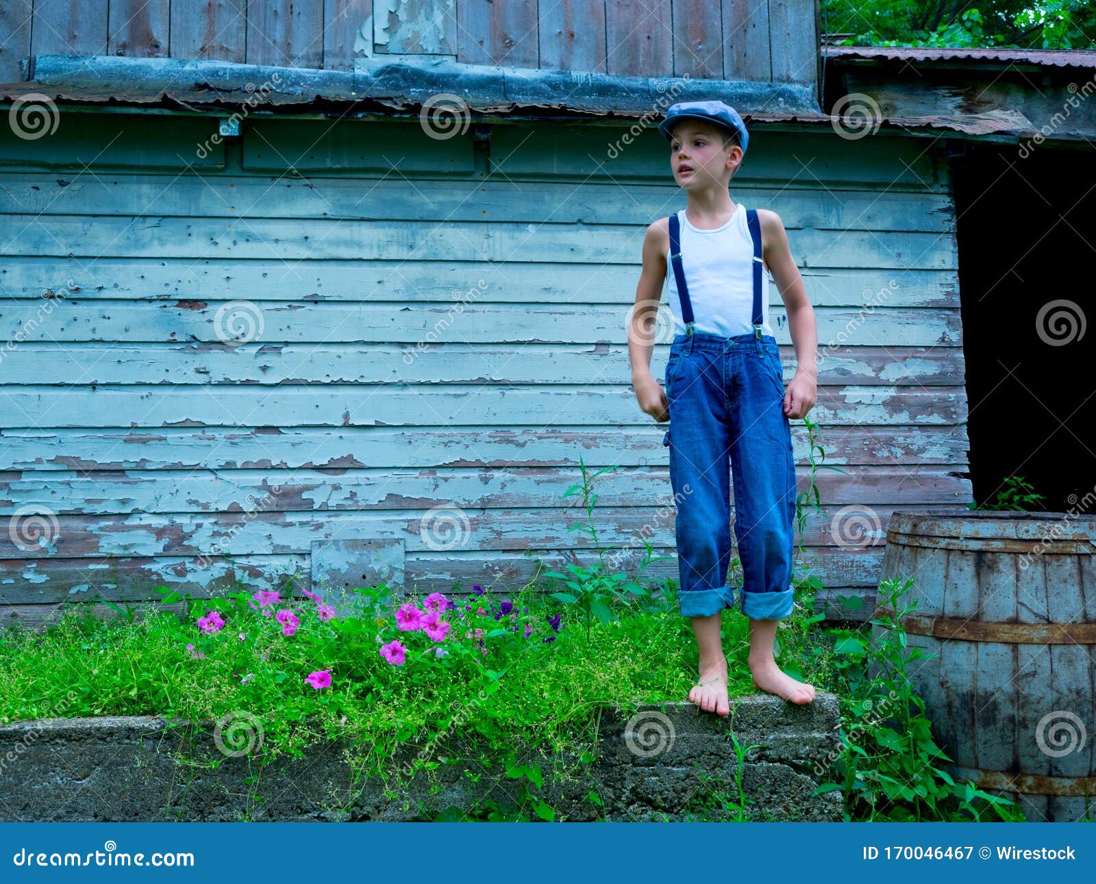 Little Boy with a Hat and Suspenders Standing on a Stone in a Garden