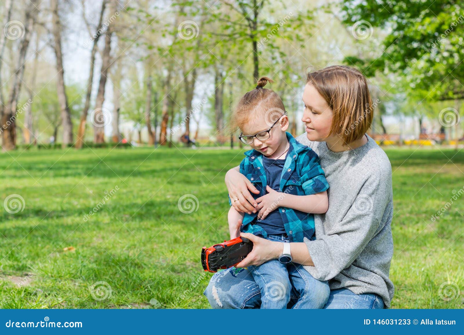 A Little Boy And His Mom Play With A Toy Car In The Park In Spring