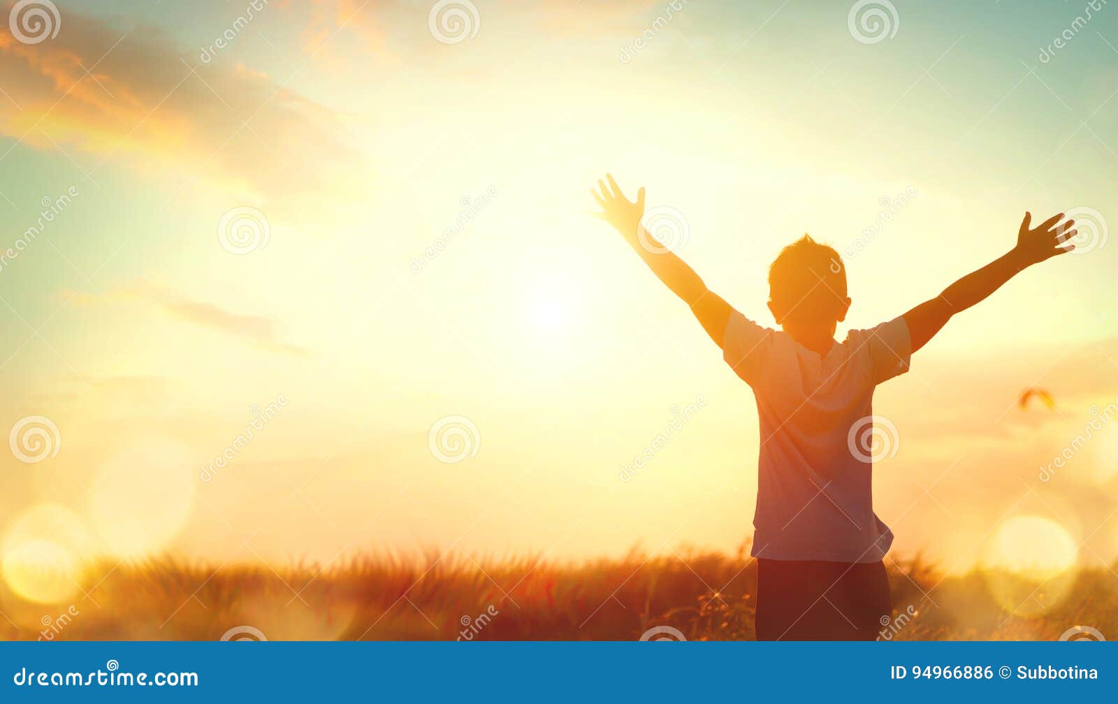 little boy raising hands over sunset sky