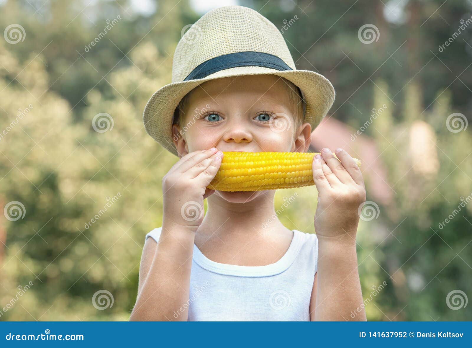 Little Boy in Straw Hat Eat Corn on the Cob in the Garden. Stock Photo