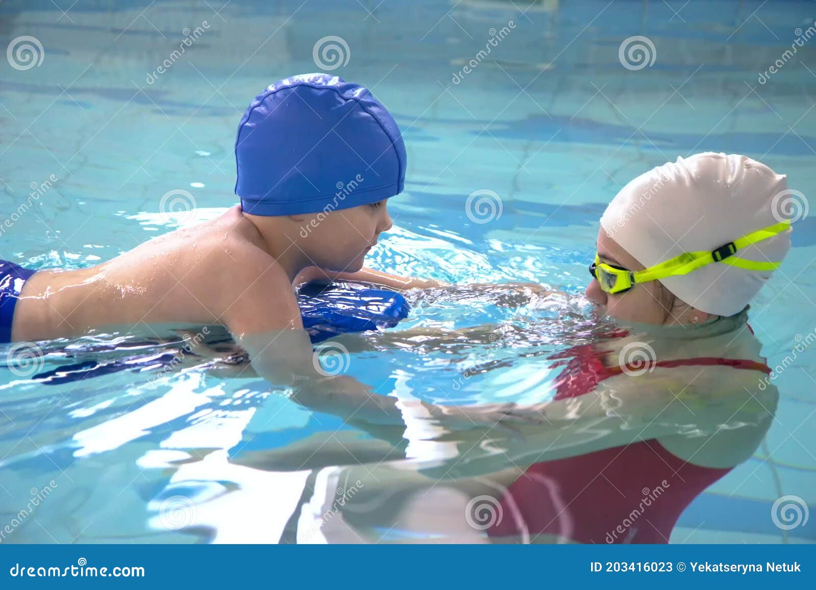 Little Boy Using the Kickboard for Learning To Swim with Trainer in the