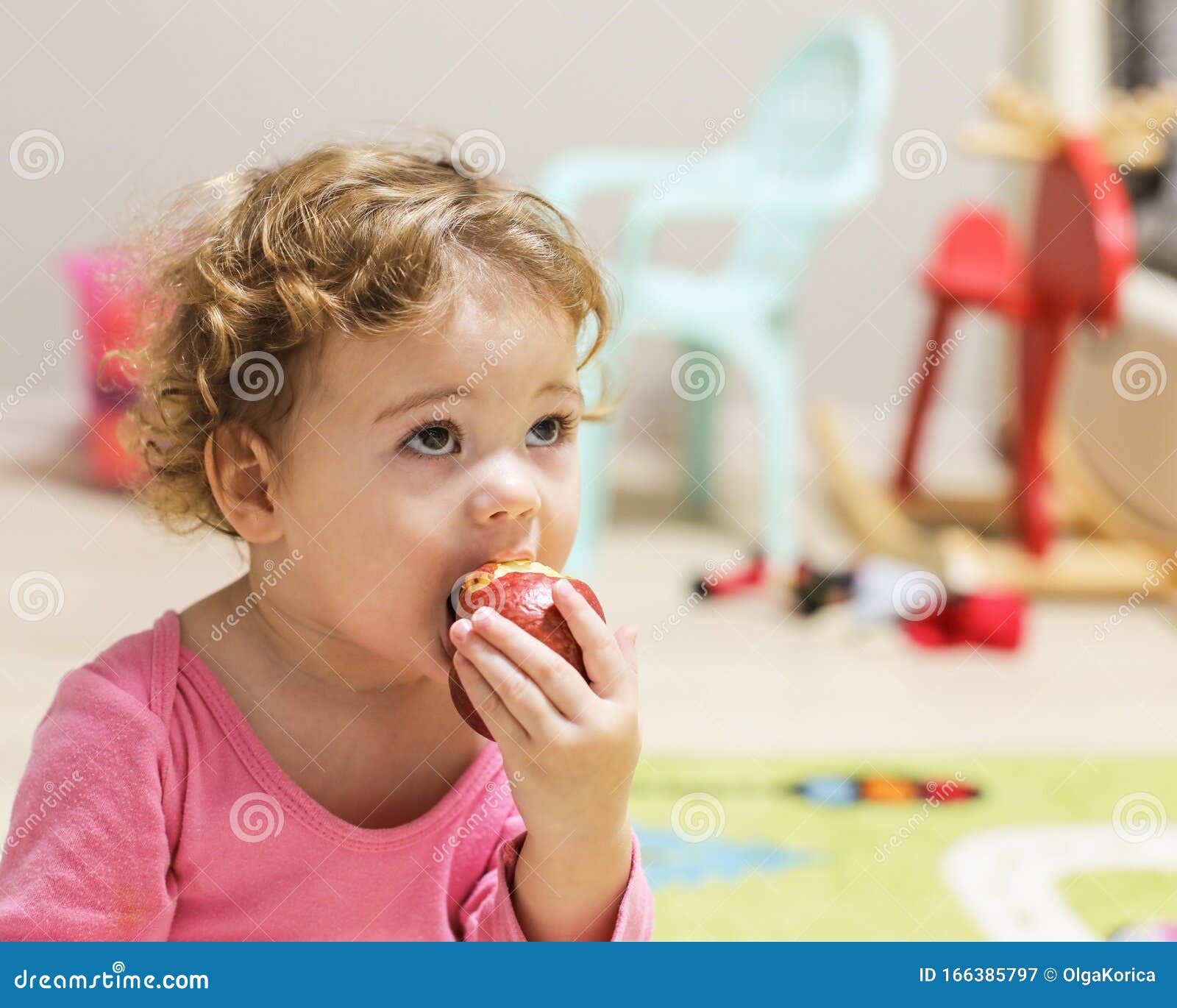 Little Caucasian Baby Girl in Pink Bites an Apple. a Child with Curly Short  Hair in the Home Interior, Portrait of a Girl Stock Image - Image of  european, little: 166385797