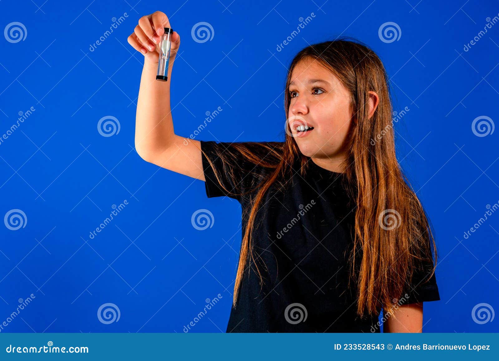 little caucasian girl holding an hourglass over blue estudio background