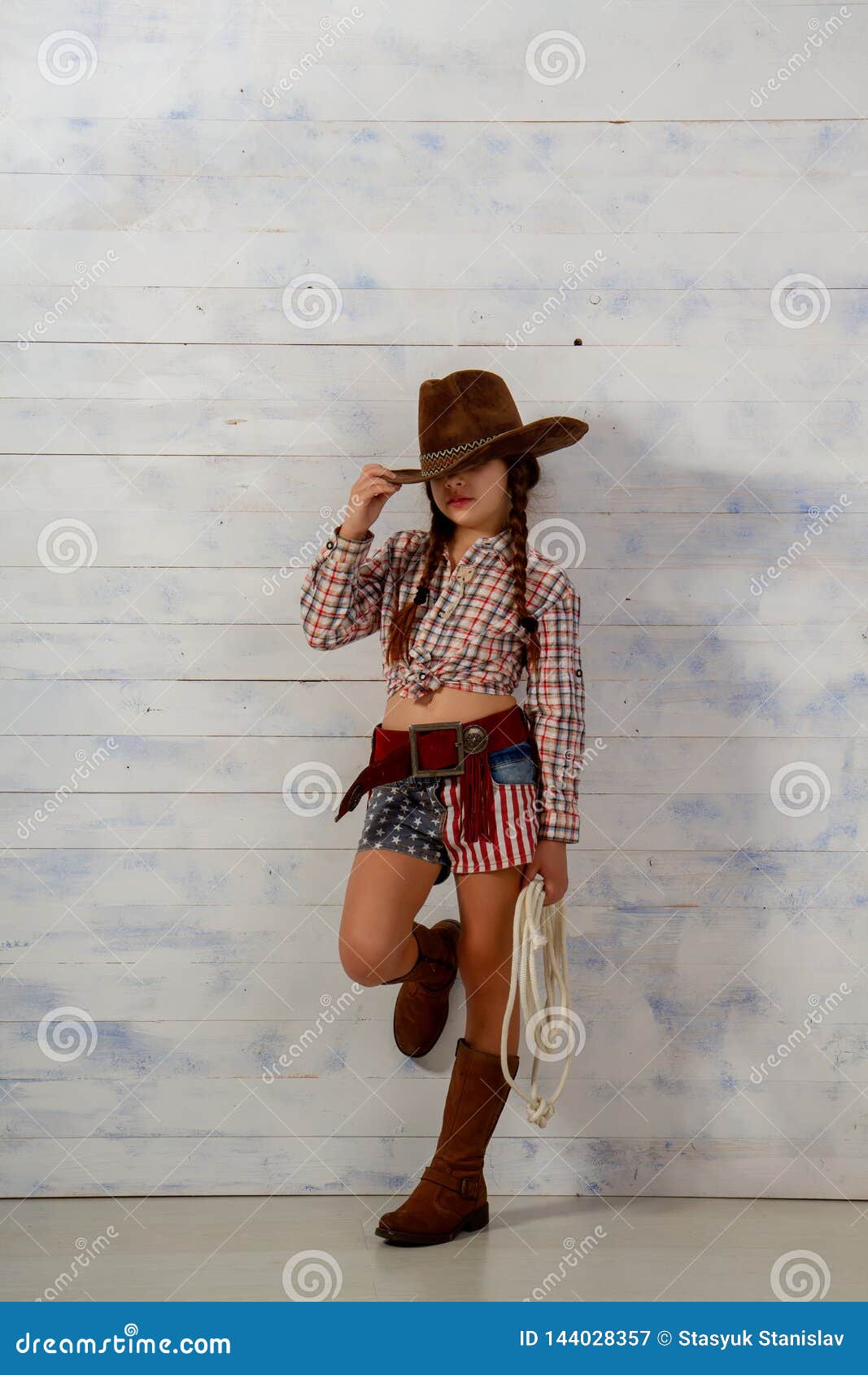 little cowboy girl wide brimmed hat traditional dress high boots lasso posing light wooden background 144028357