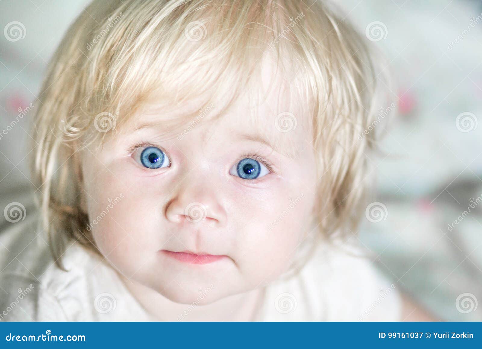 A little cute baby with blue eyes. A child with blue eyes. A bright picture of a girl with blond hair. Care for the child. Happy child smiling. Carefree childhood. Joyful look of the kid.