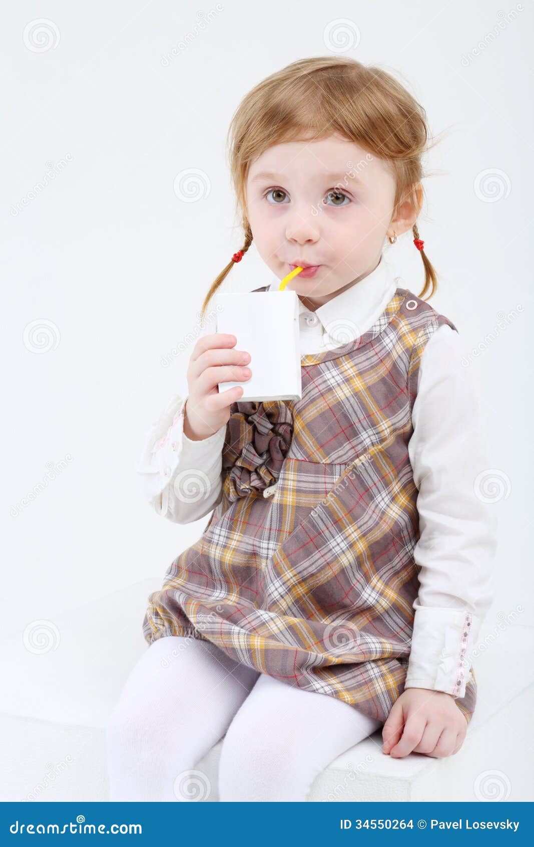 Little cute girl sits and drinks sweet juice on white background.