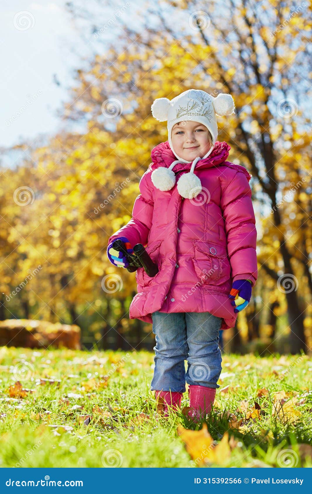 little girl with binocular stands on grassy glade