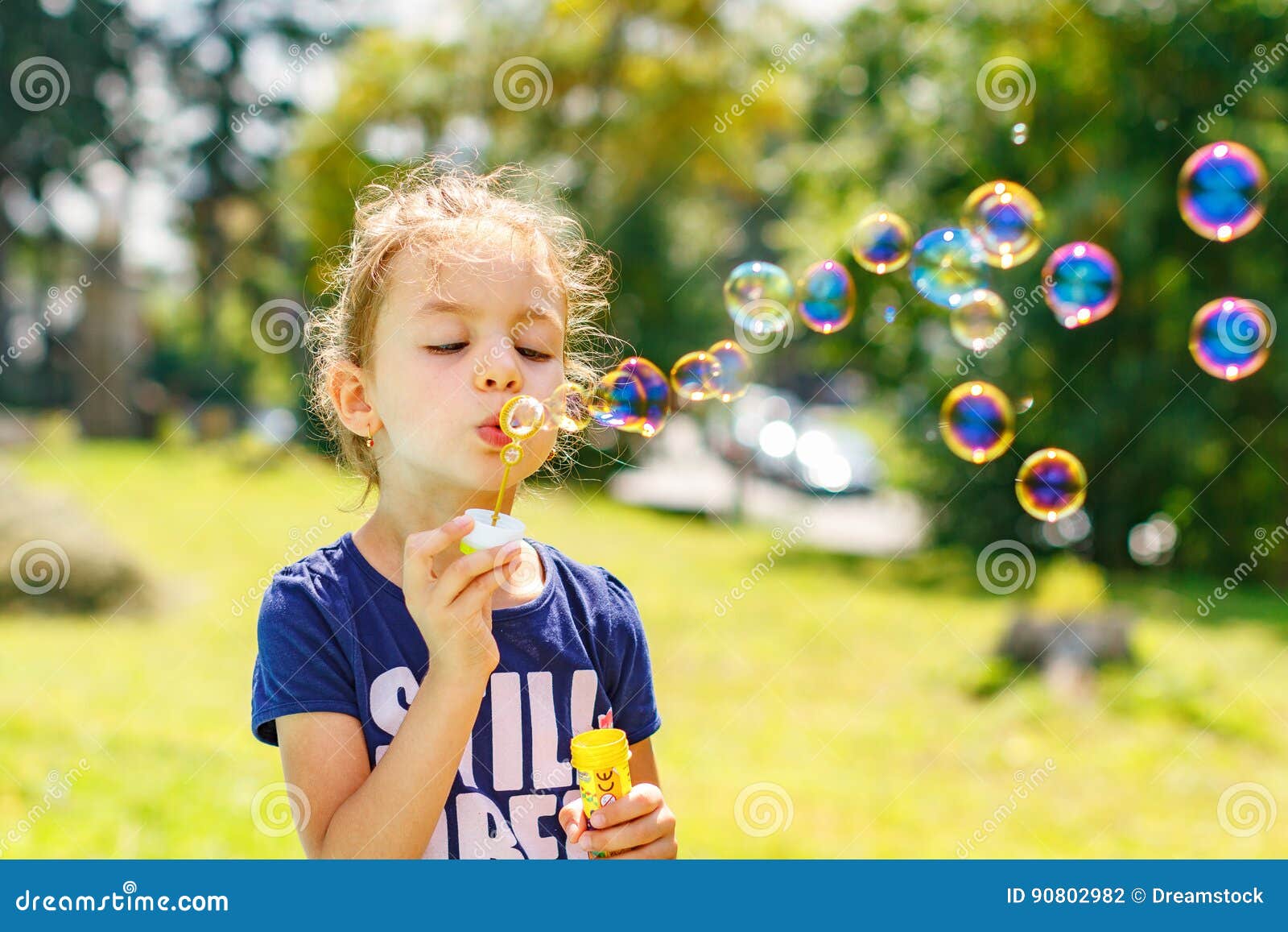 a little girl blowing soap bubbles in summer park.