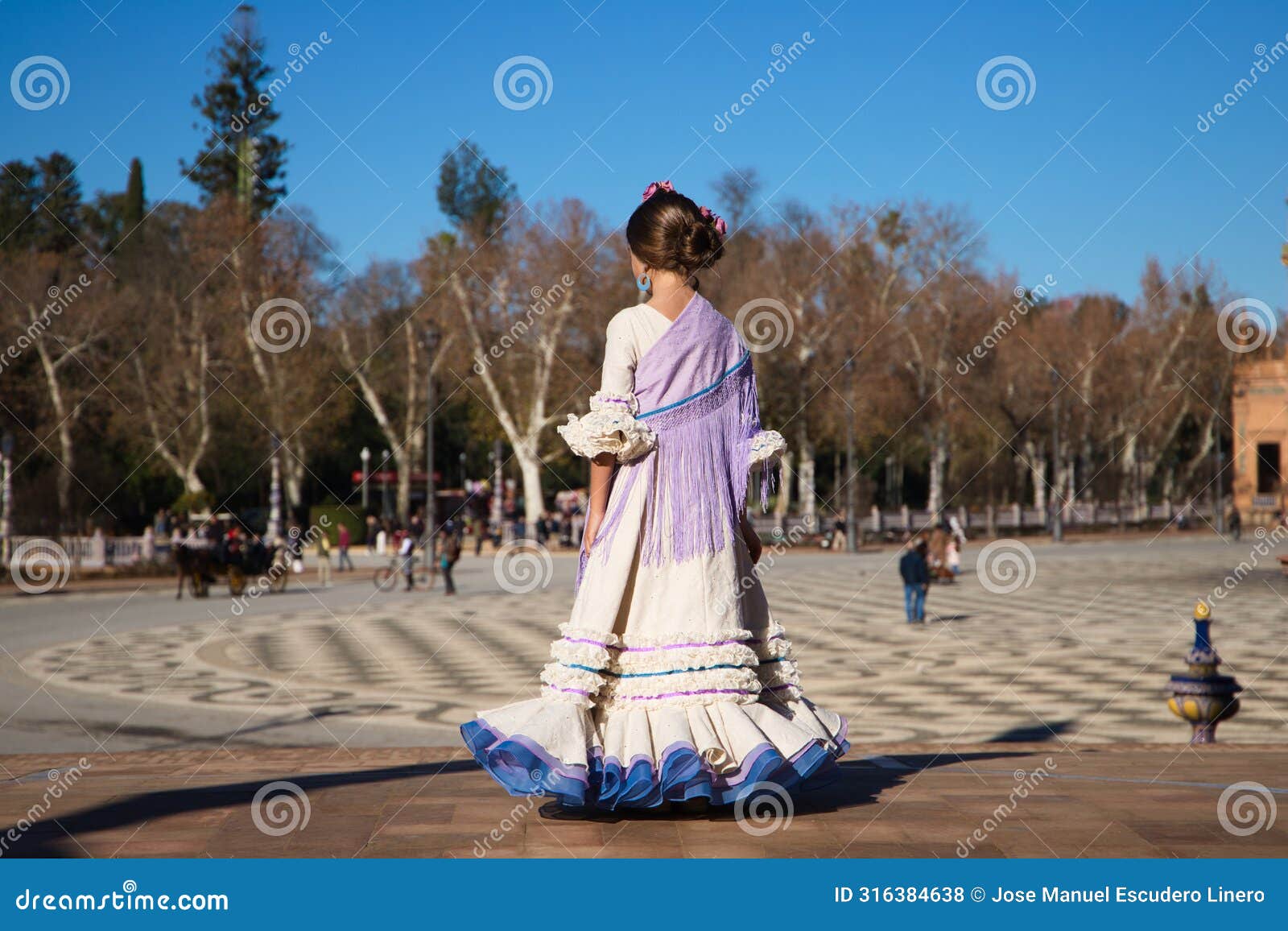 a little girl dancing flamenco dressed in a beige dress with ruffles and purple fringes in a famous square in seville, spain. the
