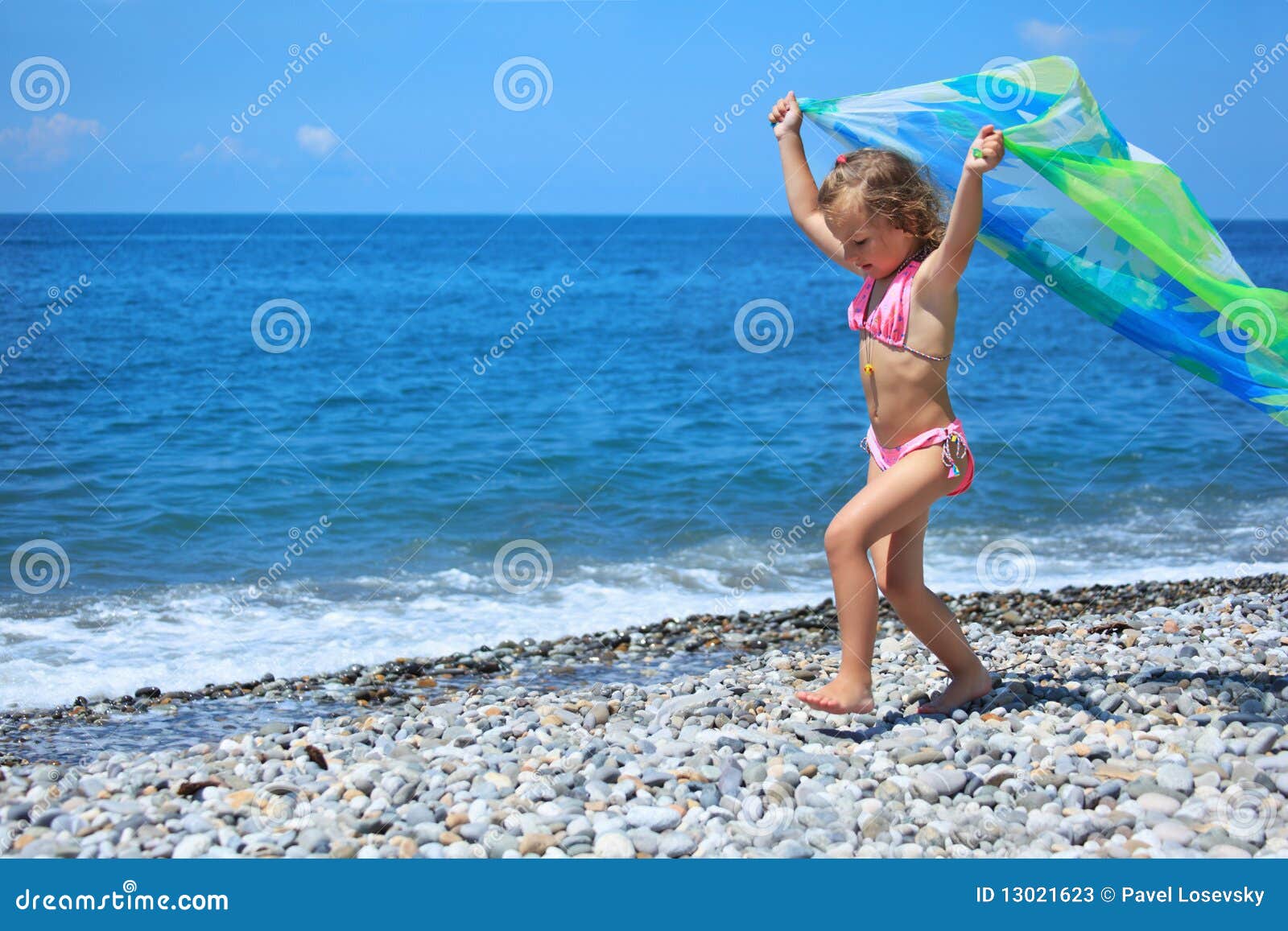 little girl with fabric on stony seacoast