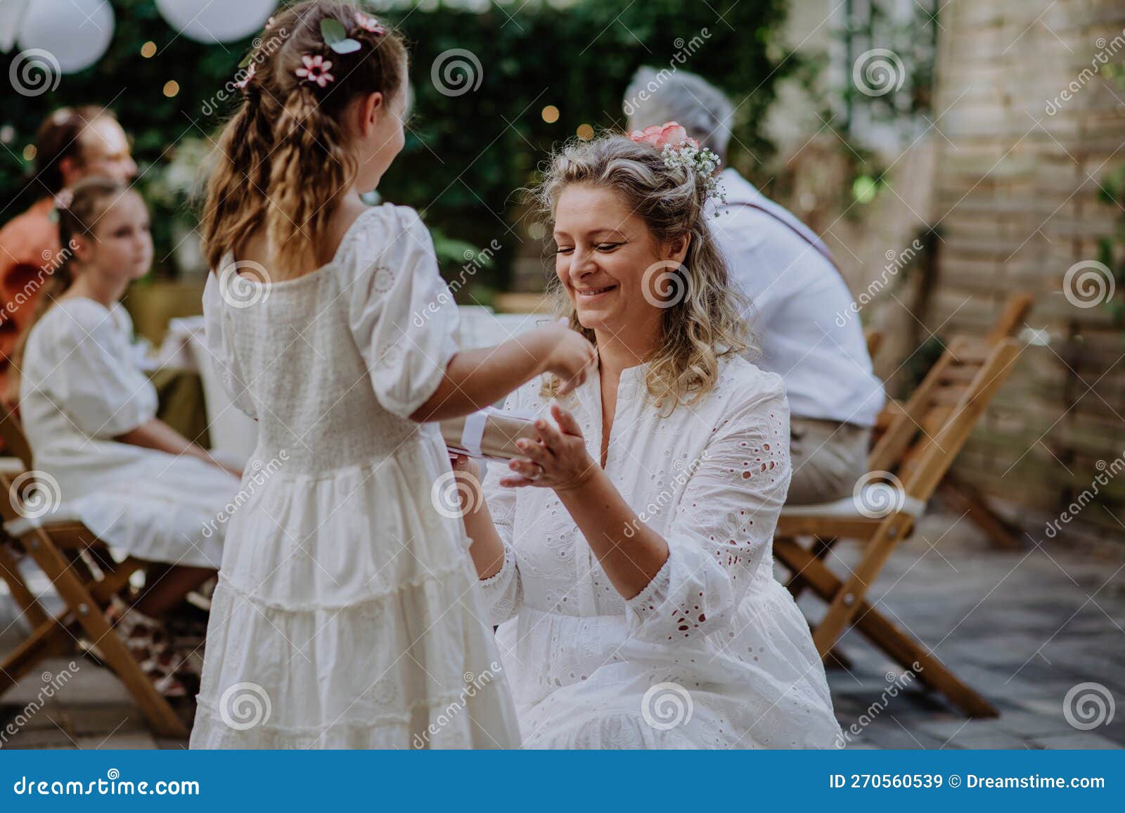 little girl giving wedding gift to mature bride at wedding backyard party.