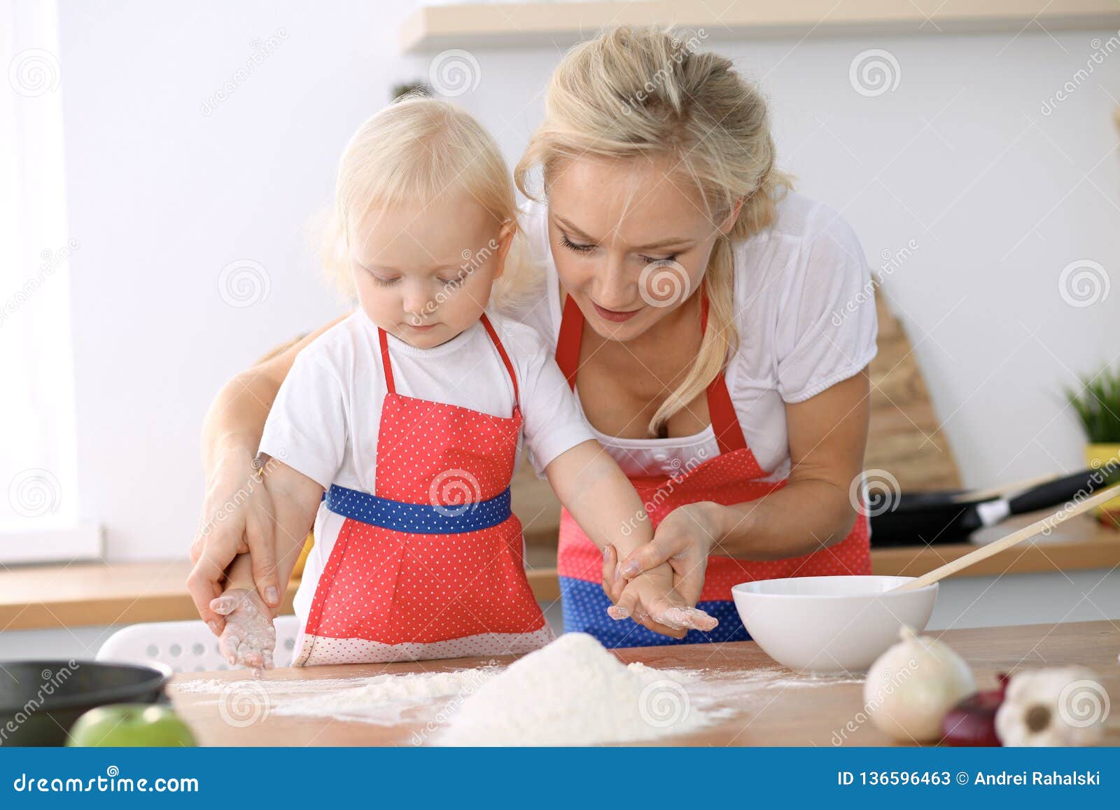 Little Girl And Her Blonde Mom In Red Aprons Playing And Laughing