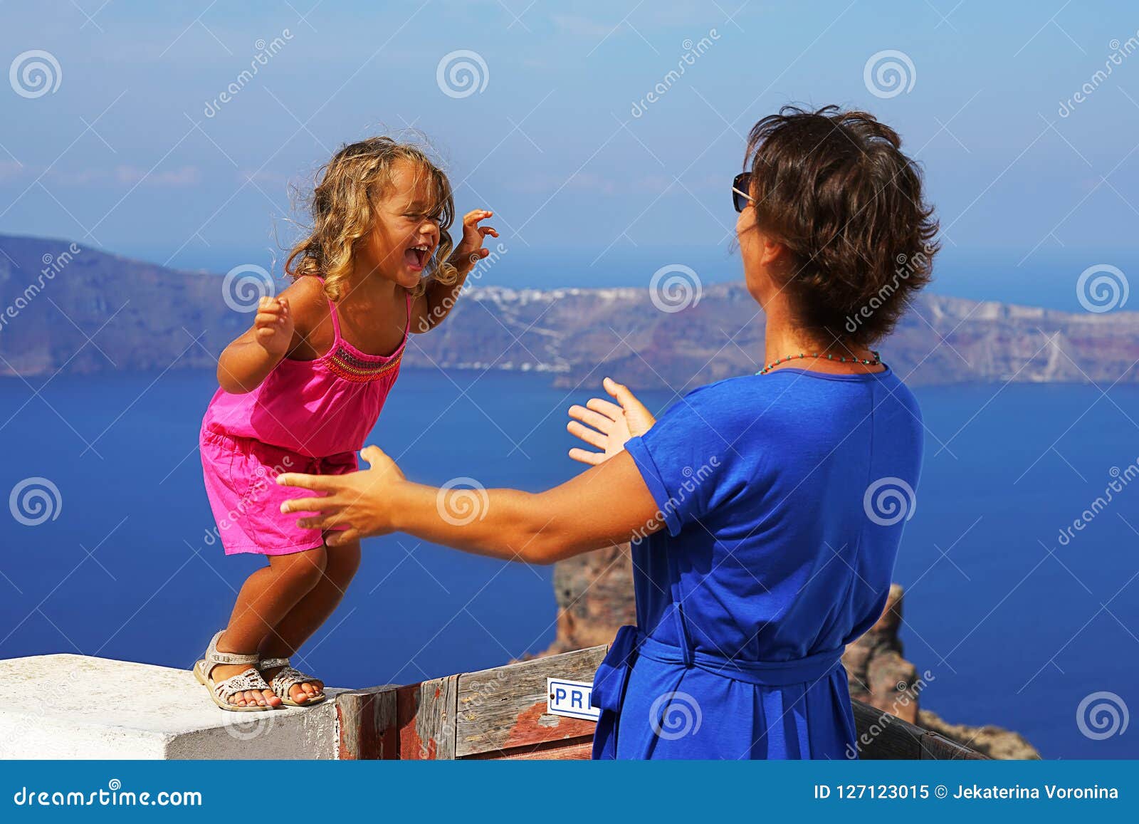 little girl jumping into the arms of mom against the nice view of santorini