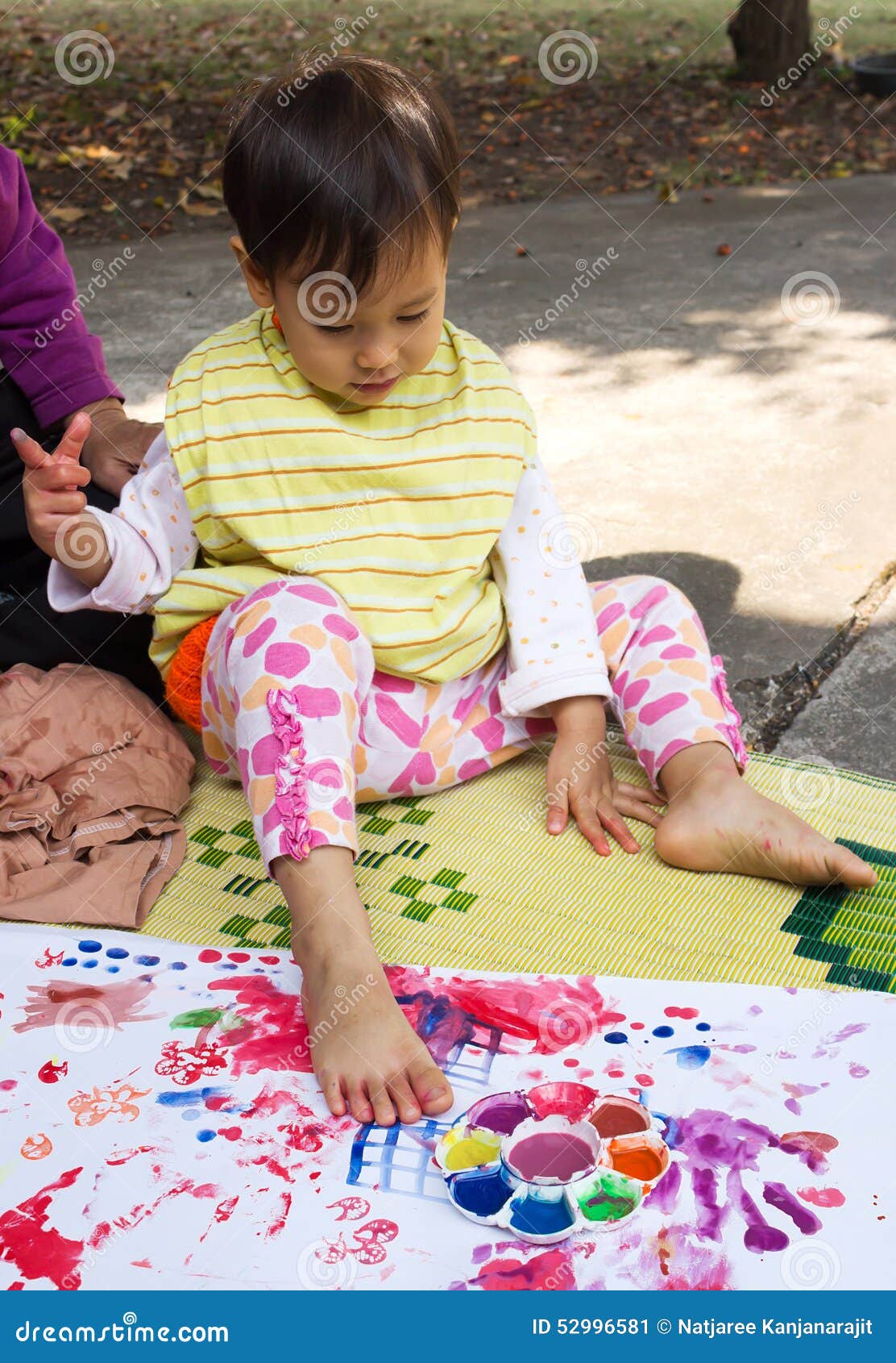 Little girl painting on white paper. Little girl put feet on white paper for painting. Lifestyle and outdoor.