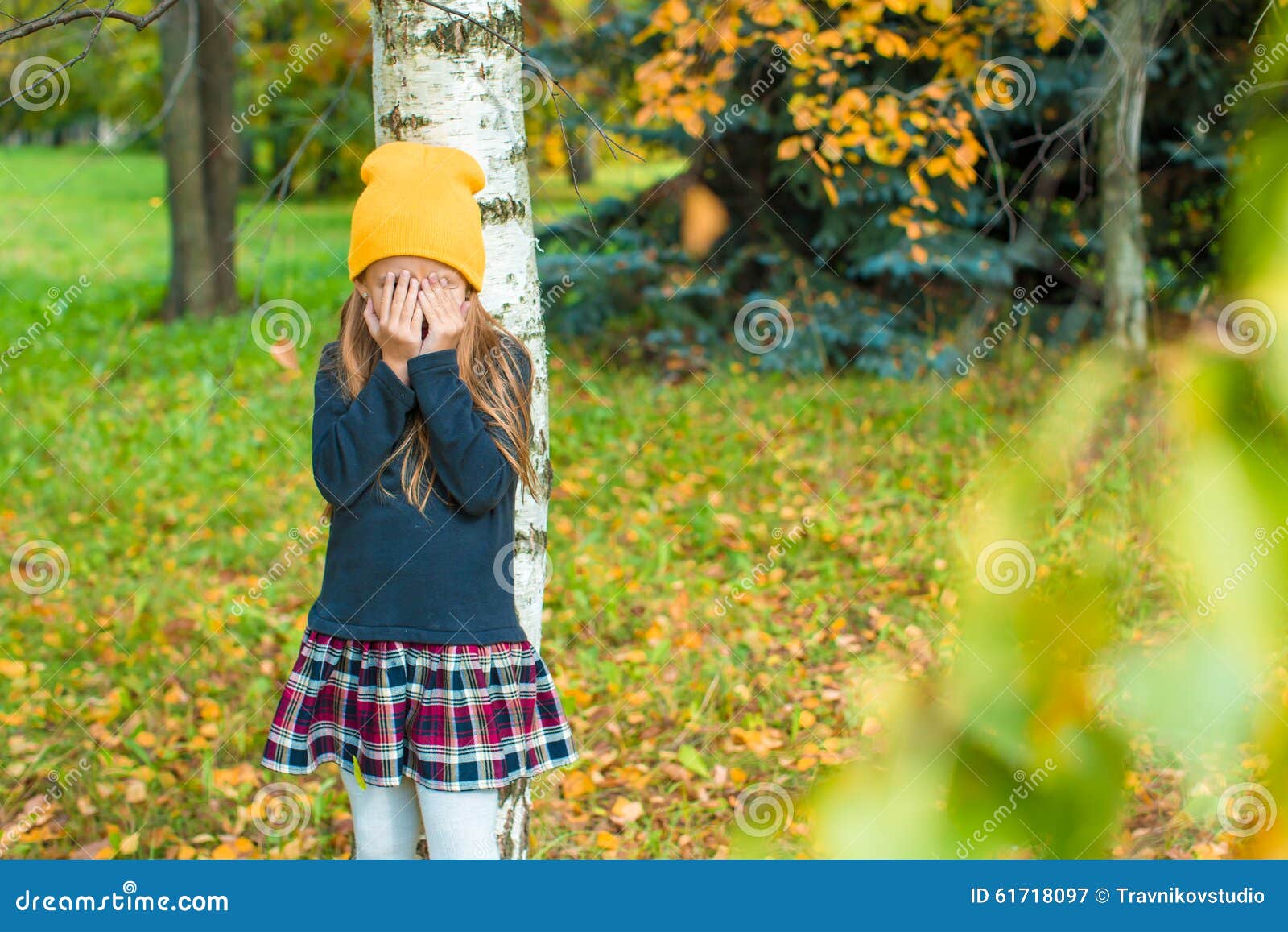 little girl playing hide and seek near tree in