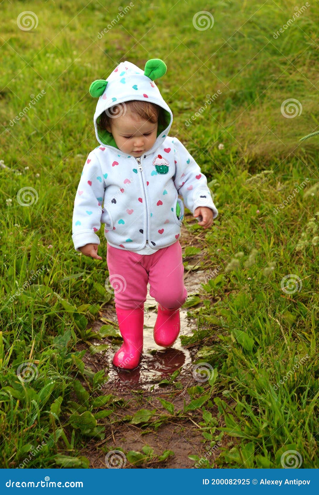 Little Girl in Red Boots Walks Along Path with Rain Puddles Stock Image