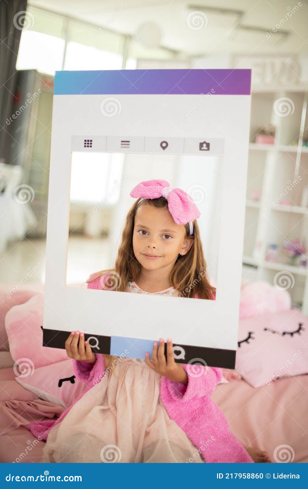little girl sitting on bed in bathrobe and lookin g at camera. holding the frame