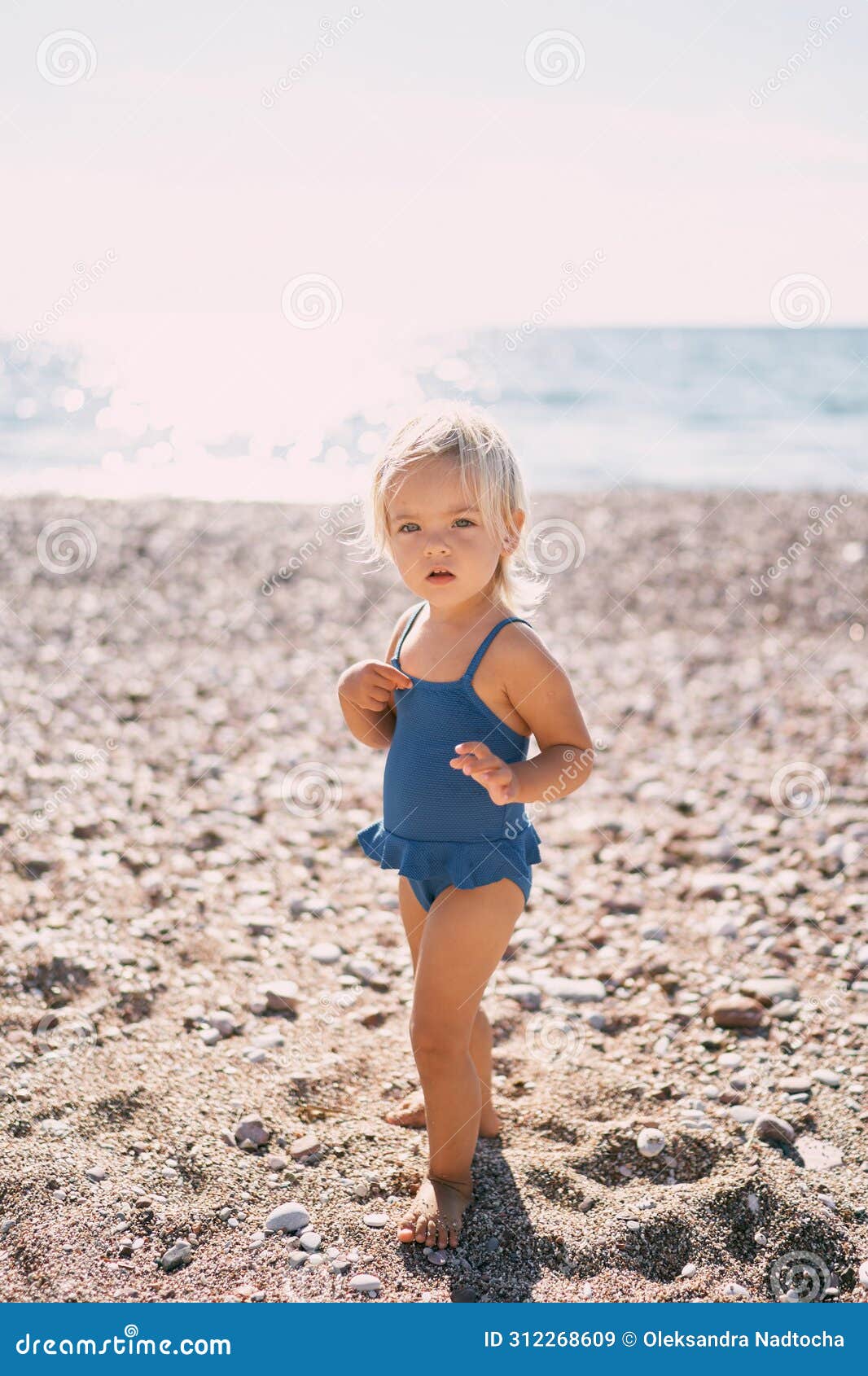 Little Girl in a Swimsuit Stands on the Beach Against the Backdrop of ...