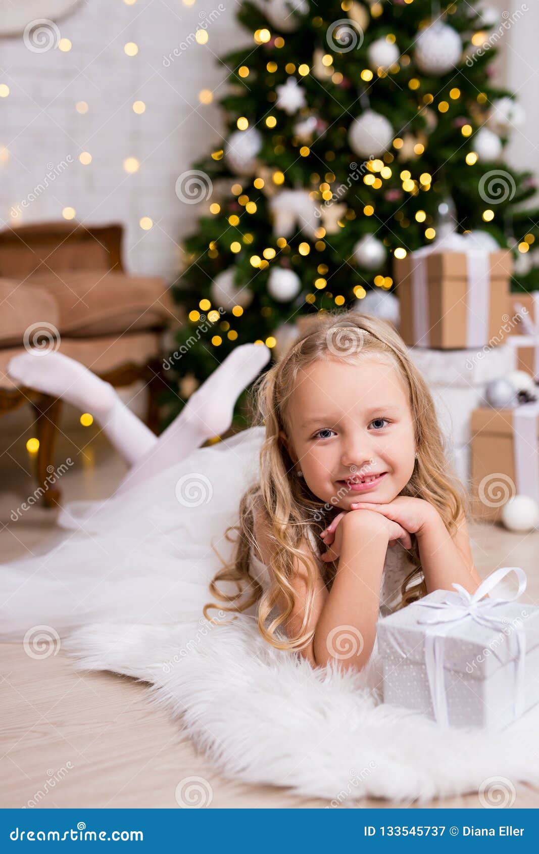 Little Girl In White Dress At Home With Christmas Tree And Gifts Stock