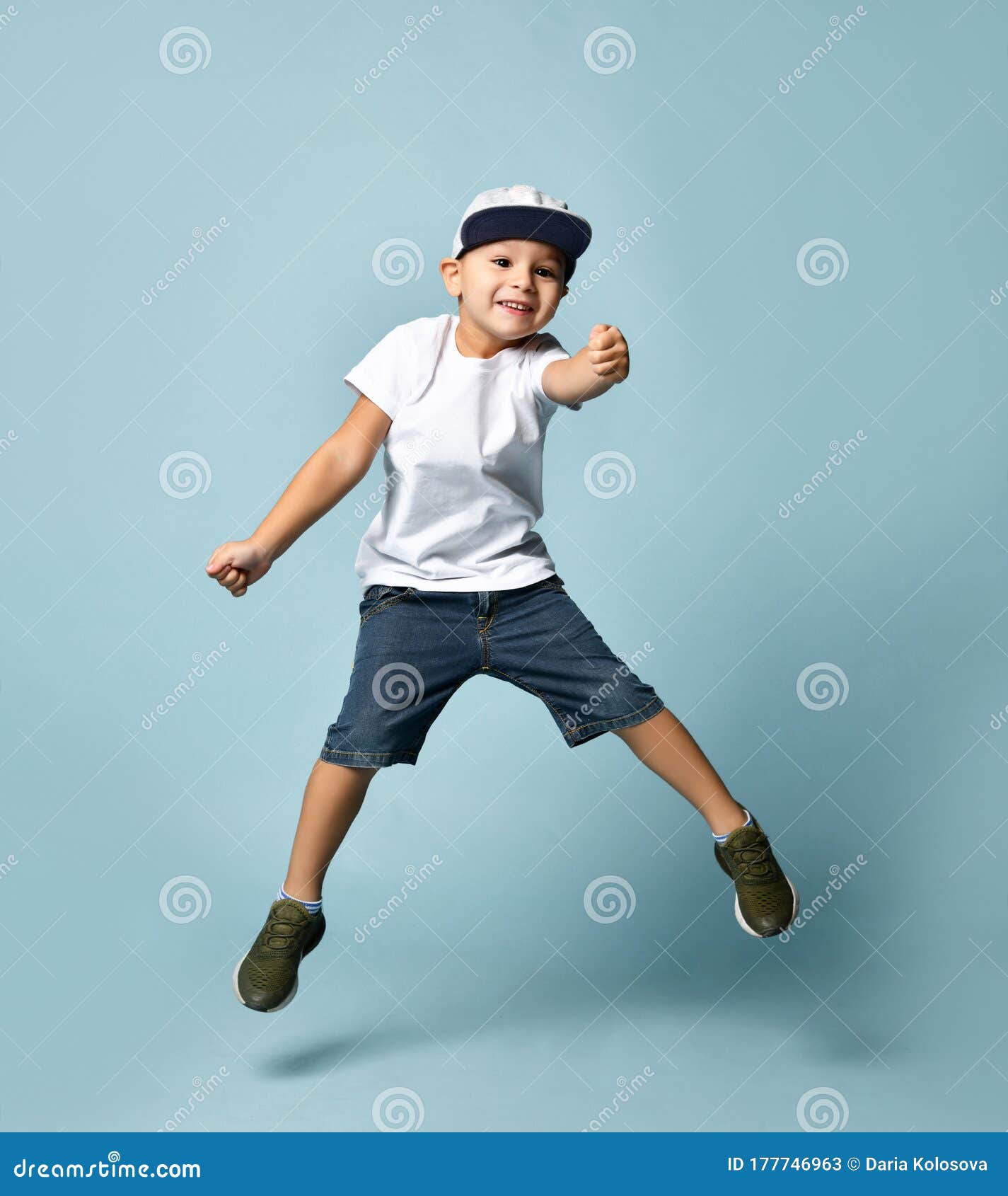 Cute baby in blue jeans, white t-shirt and denim baseball cap sits isolated  on white background Stock Photo