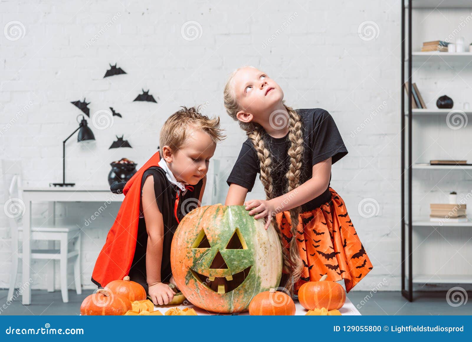 Halloween Costumes In Stock Near Me - Little Kids In Halloween Costumes Near Table With Pumpkins Stock Photo Halloween Costumes In Stock Near Me - Little Kids In Halloween Costumes Near Table With Pumpkins Stock Photo
