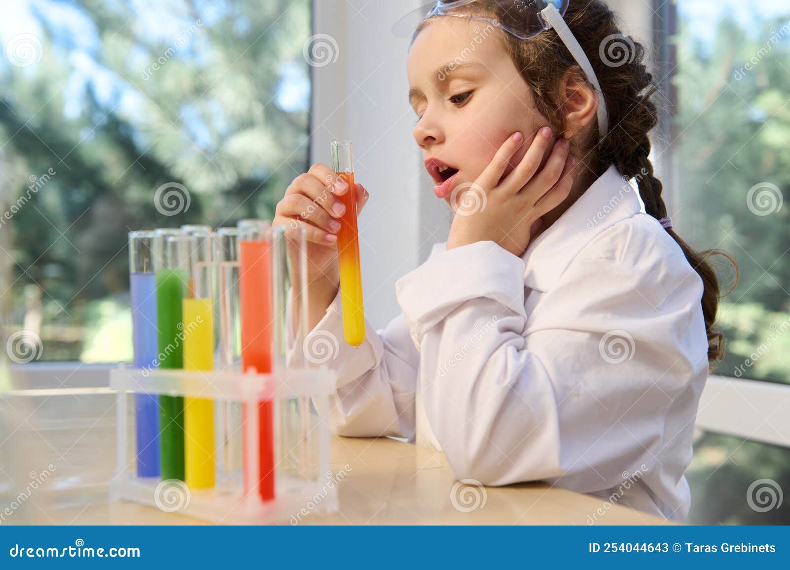 little schoolgirl observing the chemical reaction standing at the table with test tubes on tripode on a chemistry lesson