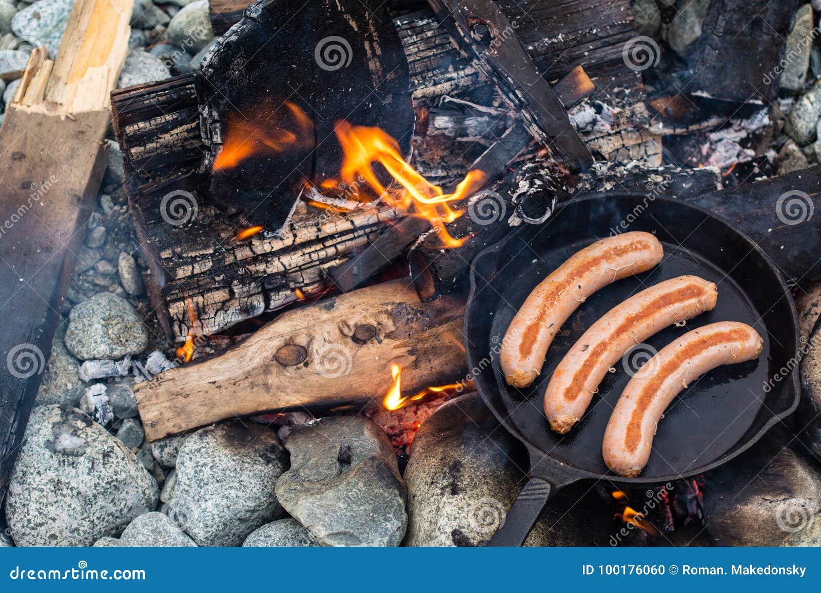 Cooking sausages in cast iron skillet on campfire while camping. Good and  positive campfire food. Stock Photo