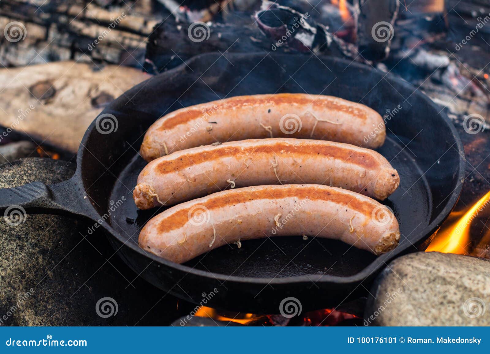 Cooking sausages in cast iron skillet on campfire while camping. Good and  positive campfire food. Stock Photo