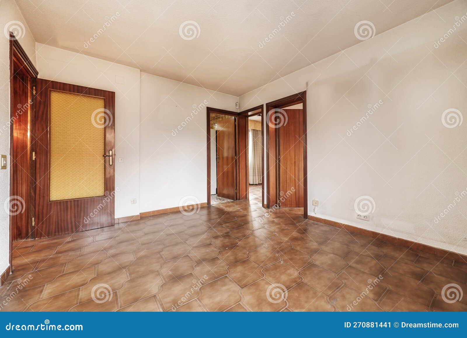 living room of an empty apartment with cheap dark wood carpentry and brown tile floors