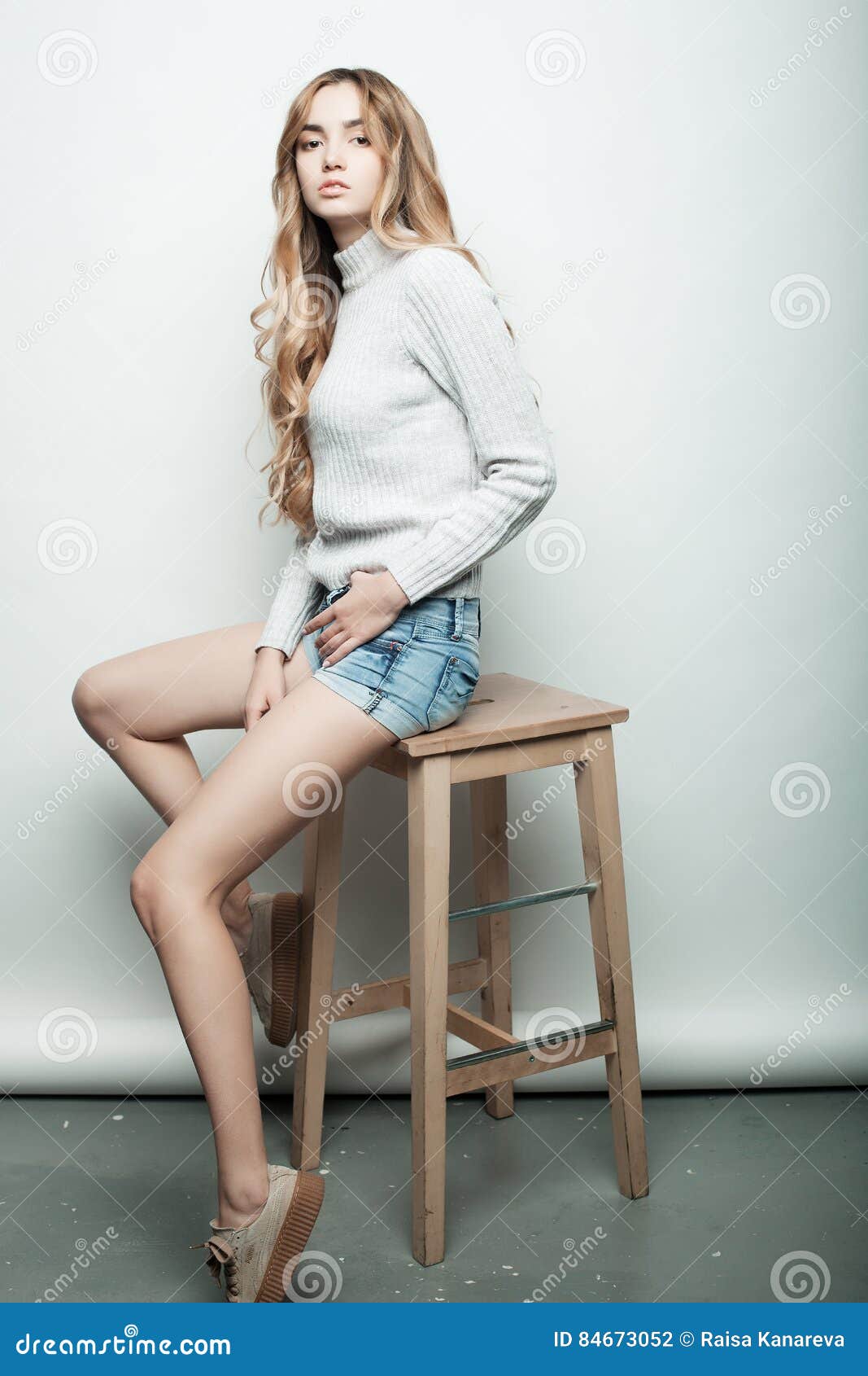 Livsstil, mode och folkbegrepp: Full kroppstående av ett kvinnligt sammanträde för modemodell på wood stol i studio