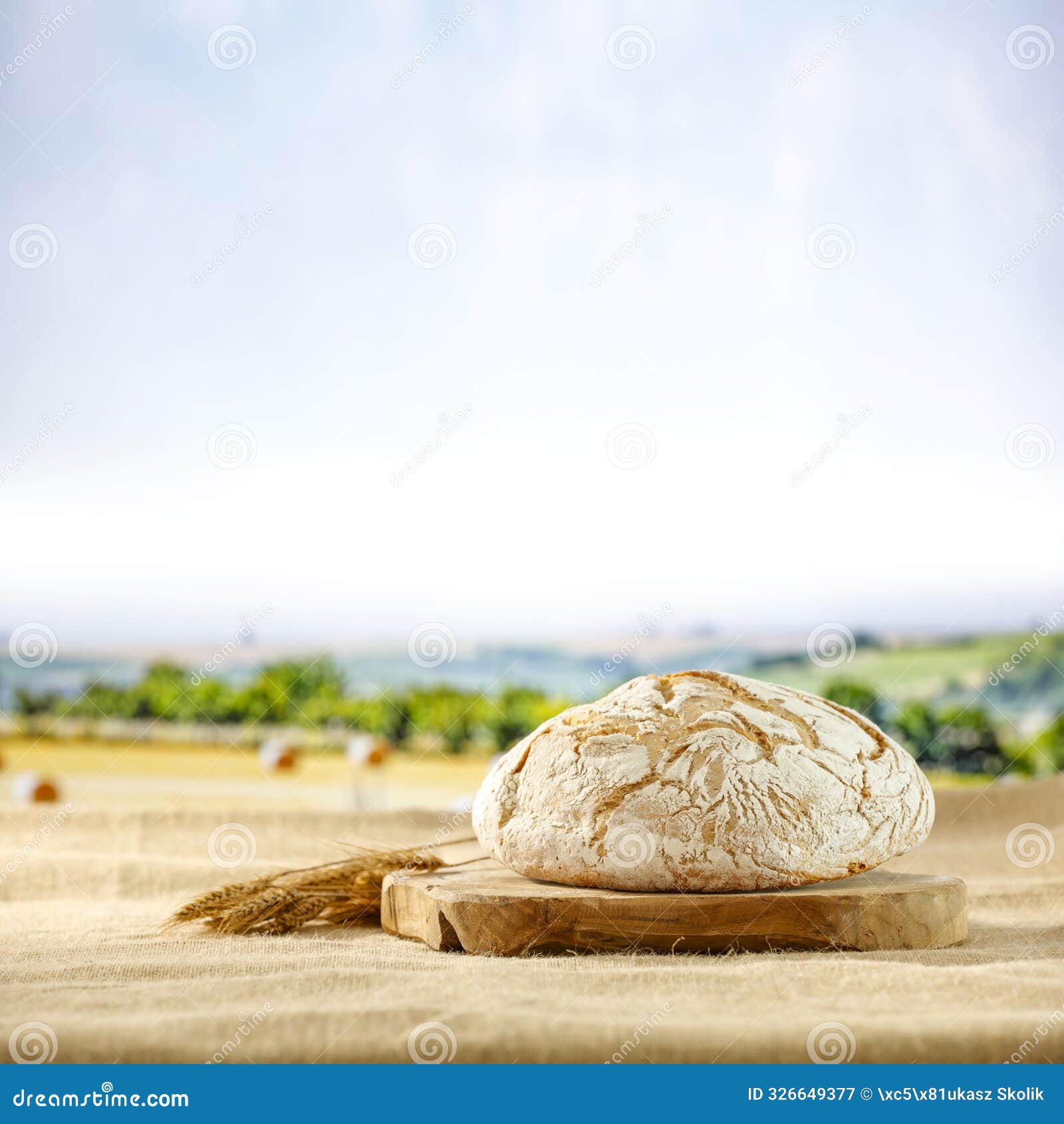 loaf of bread on canvas tablecloth on a background of summer yellow and green field and farm