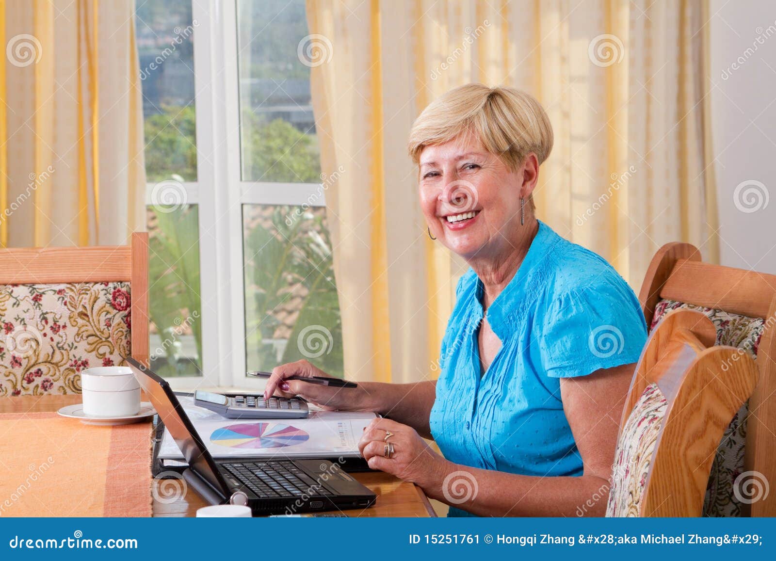 Lohnlisten einer glücklichen älteren Frau zu Hause vor Laptop und mit calcultor und Datei