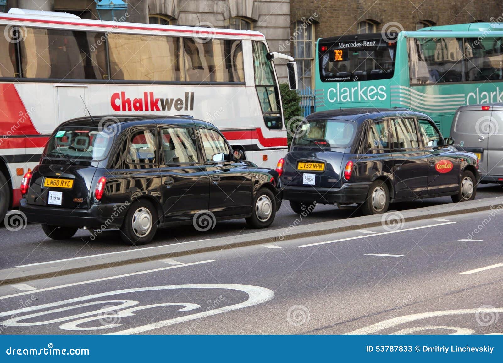 Londres ennegrece el taxi que se sigue delante de los autobuses en el camino. El tráfico de la calle de Londres con dos dos grandes autobuses del taxi negro y se está moviendo a lo largo del camino