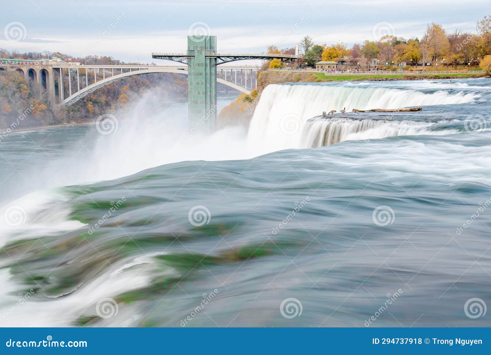 long exposure american falls waterfall cascade with gooses near niagara falls observation tower and rainbow international bridge,