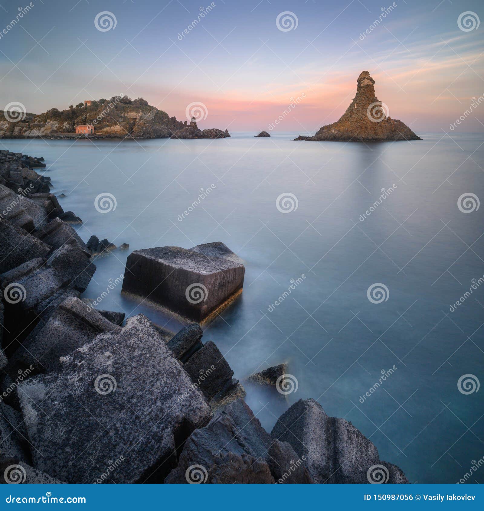 long exposure panoramic shot of the cyclope island with breakwater cube blocks at the coast of acitrezza, sicily, italy