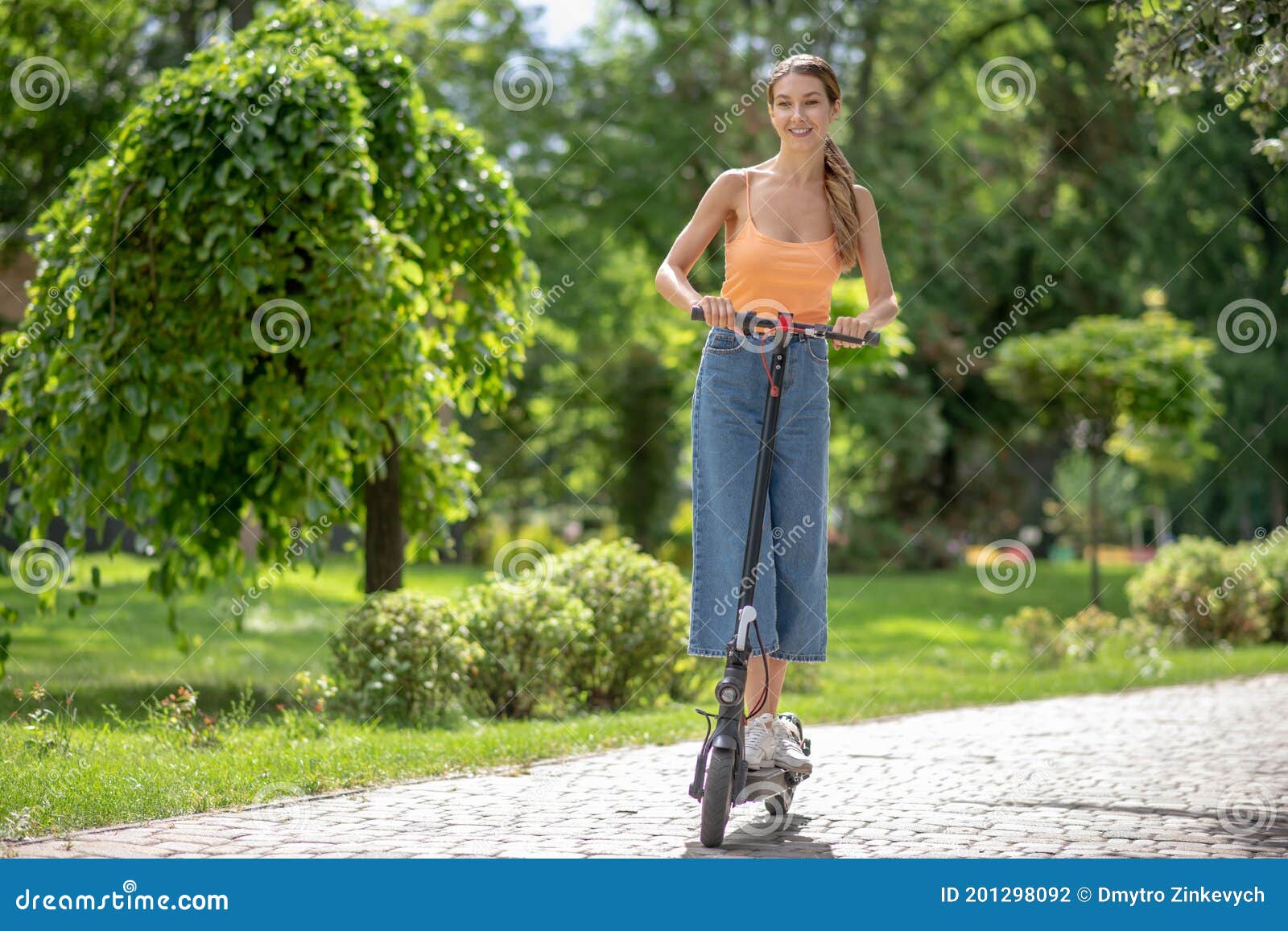 Long-haired Young Girl Riding a Scooter in the Park and Looking ...