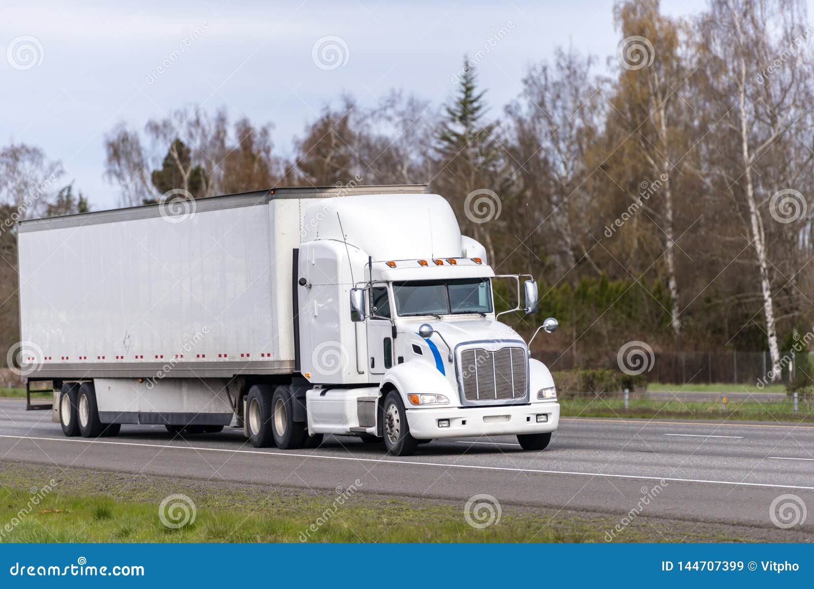 long haul white big rig semi truck transporting goods in dry van semi trailer running on straight highway road