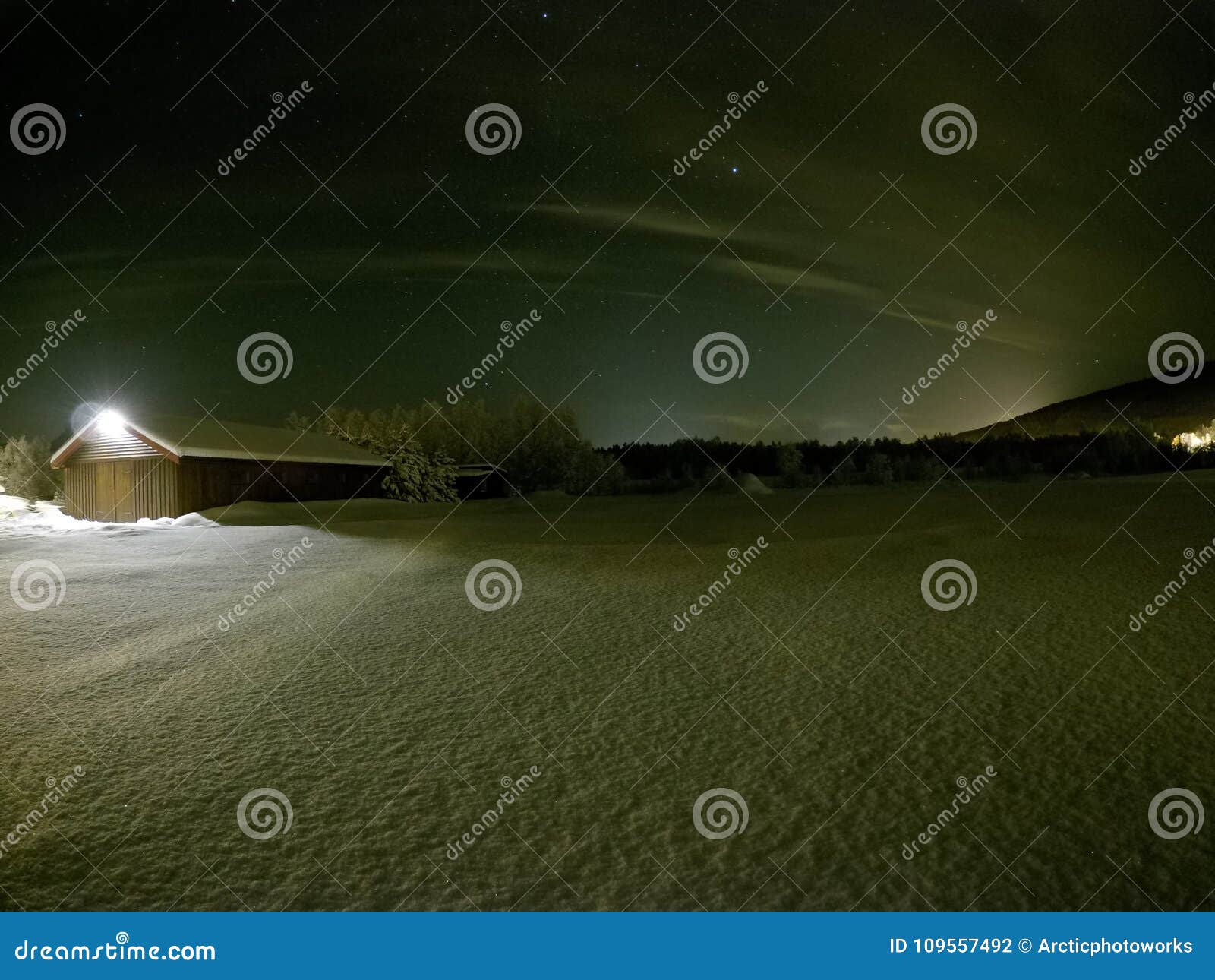 long snowy field at night with barn and ligh