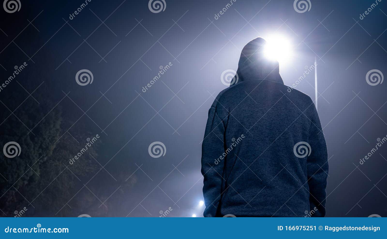 looking up from behind at a mysterious, moody, hooded figure. on a foggy winters night, with street lights behind