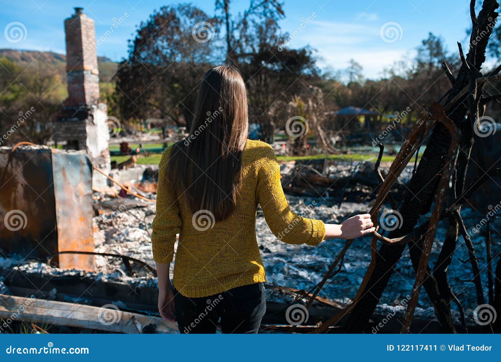 Lookinh de la mujer en su hogar quemado después del desastre del fuego. Mujer joven del dueño que comprueba la casa y la yarda quemadas y arruinadas después del fuego, consecuencias del accidente del desastre del fuego Ruinas después del desastre del fuego, de la pérdida y del concepto de la desesperación