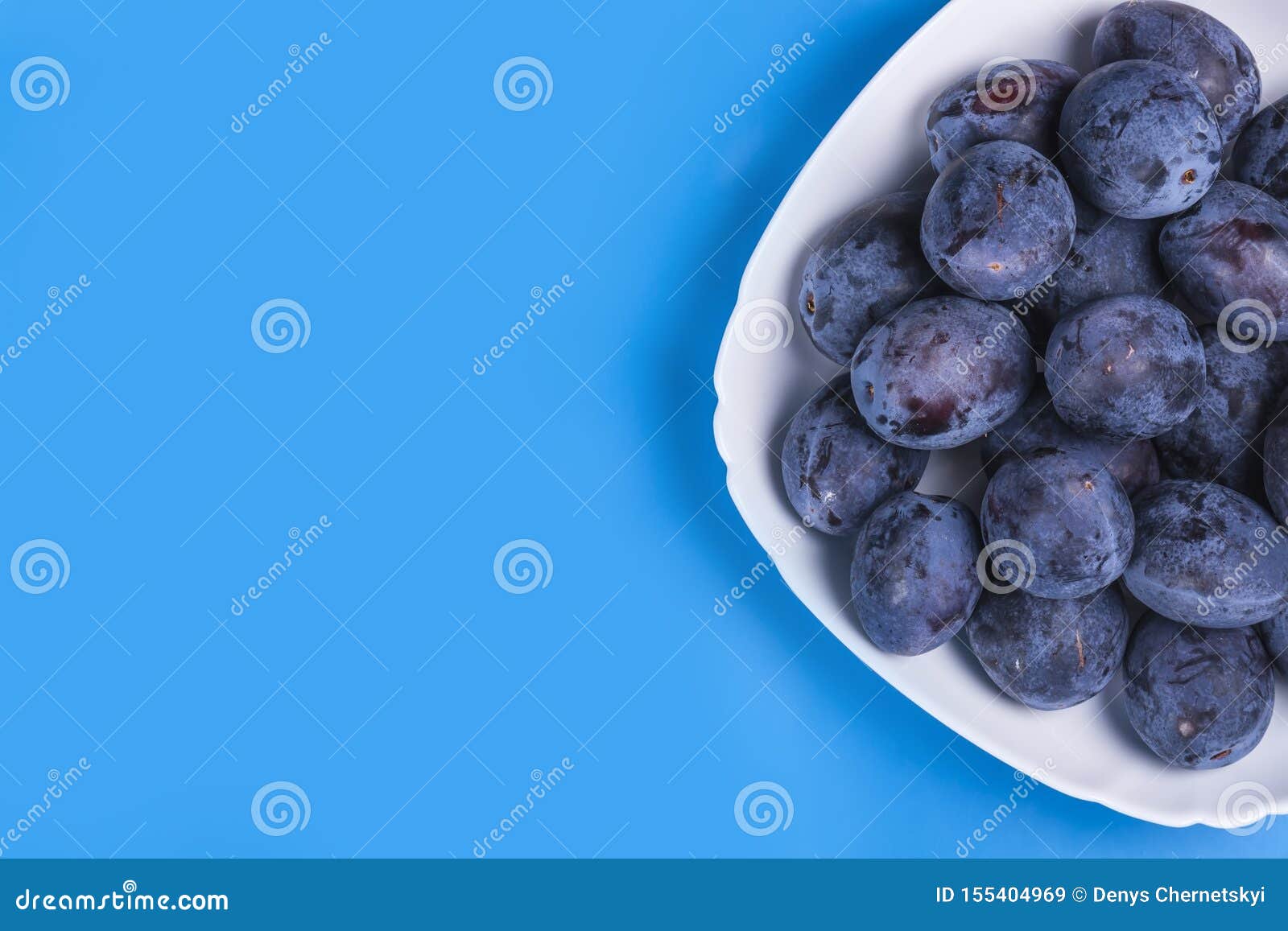 A Lot of Fresh Plums in a White Plate on a Blue Background Stock Image