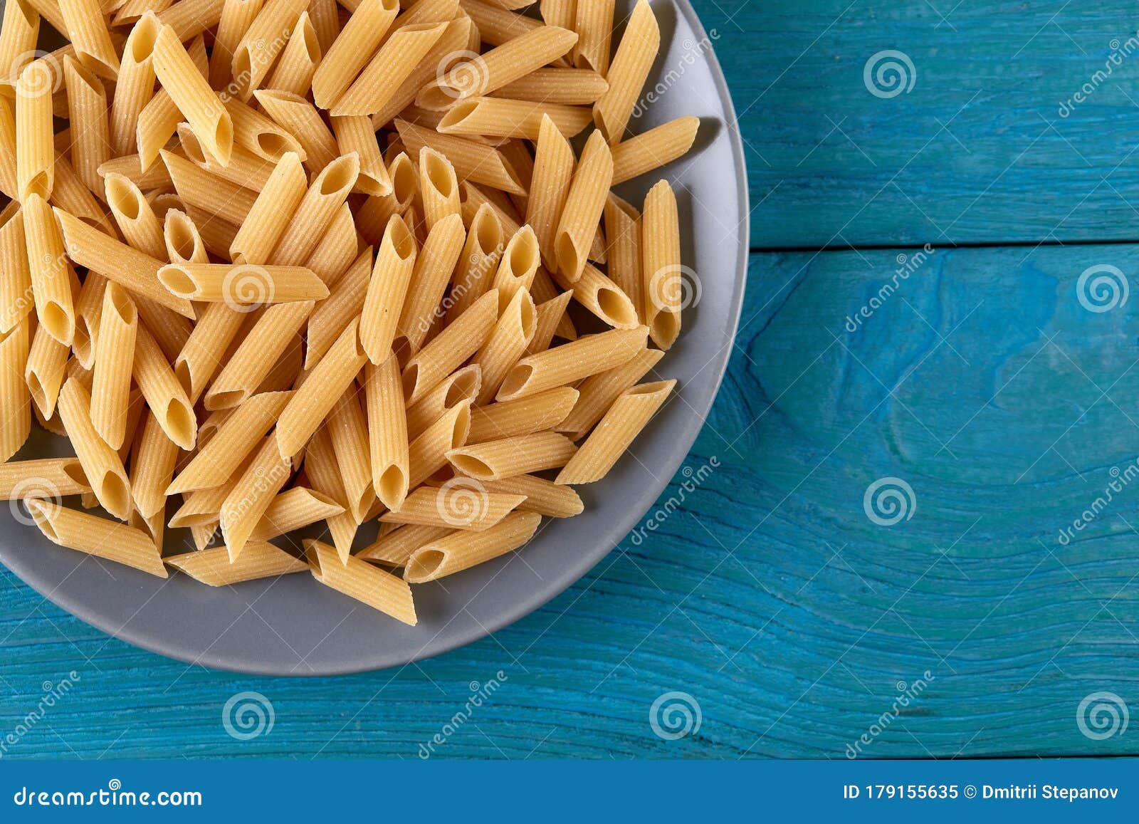 a lot of raw pasta penne on a patr of plate at blue wooden background