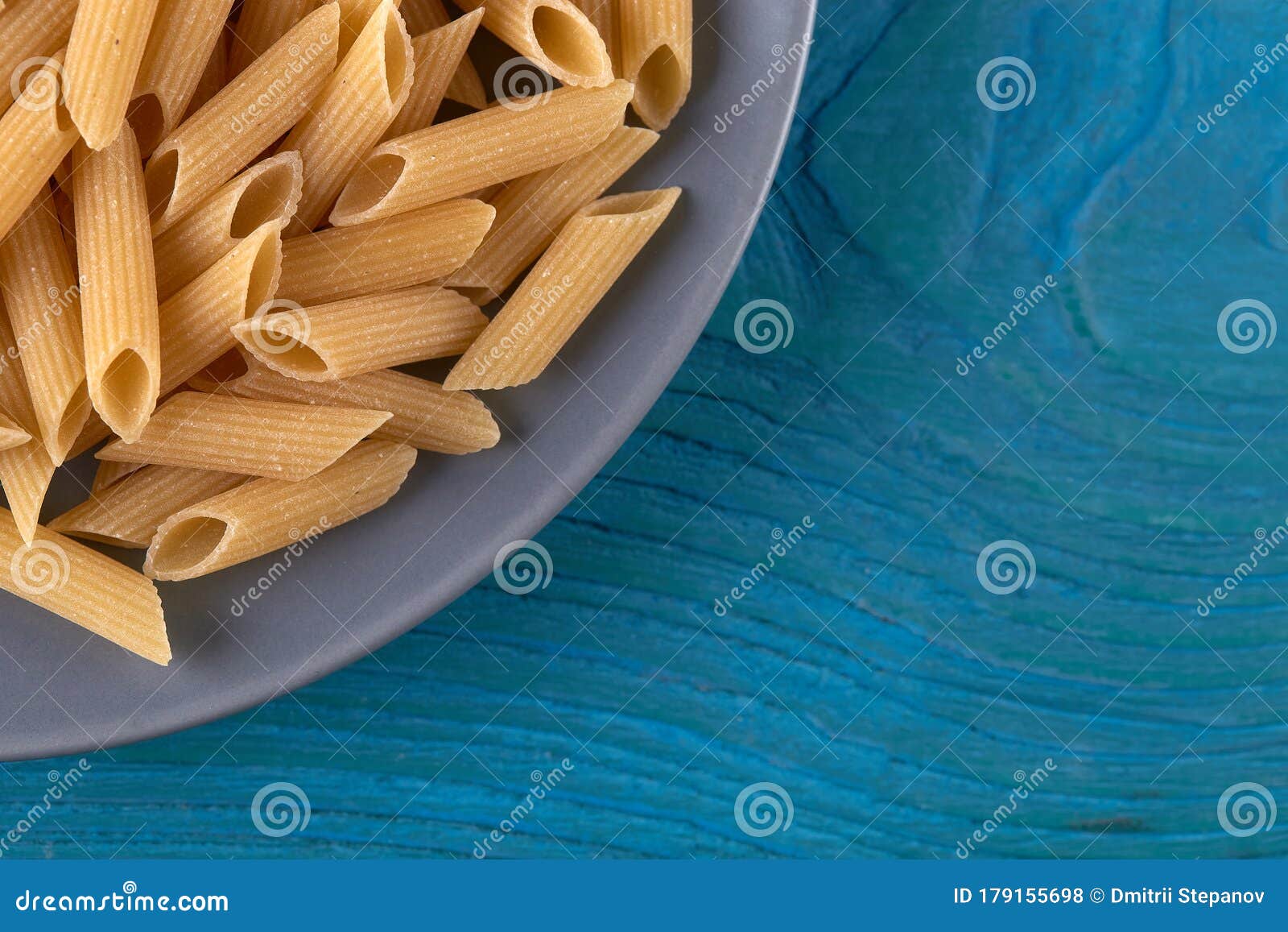 a lot of raw pasta penne on a patr of plate at blue wooden background