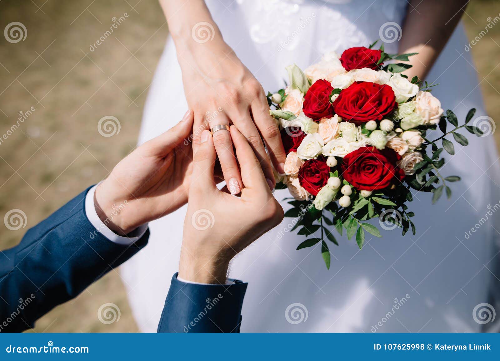 love and marriage. fine art rustic wedding ceremony outside. groom putting golden ring on the bride`s finger. bouquet of red and
