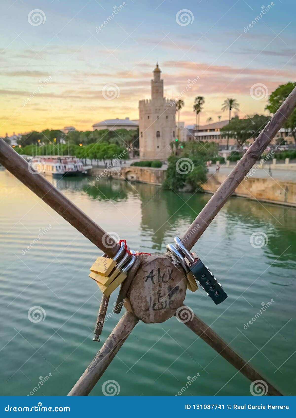 love padlocks on seville bridge with golden tower torre del oro and the guadalquivir river in the background at sunset