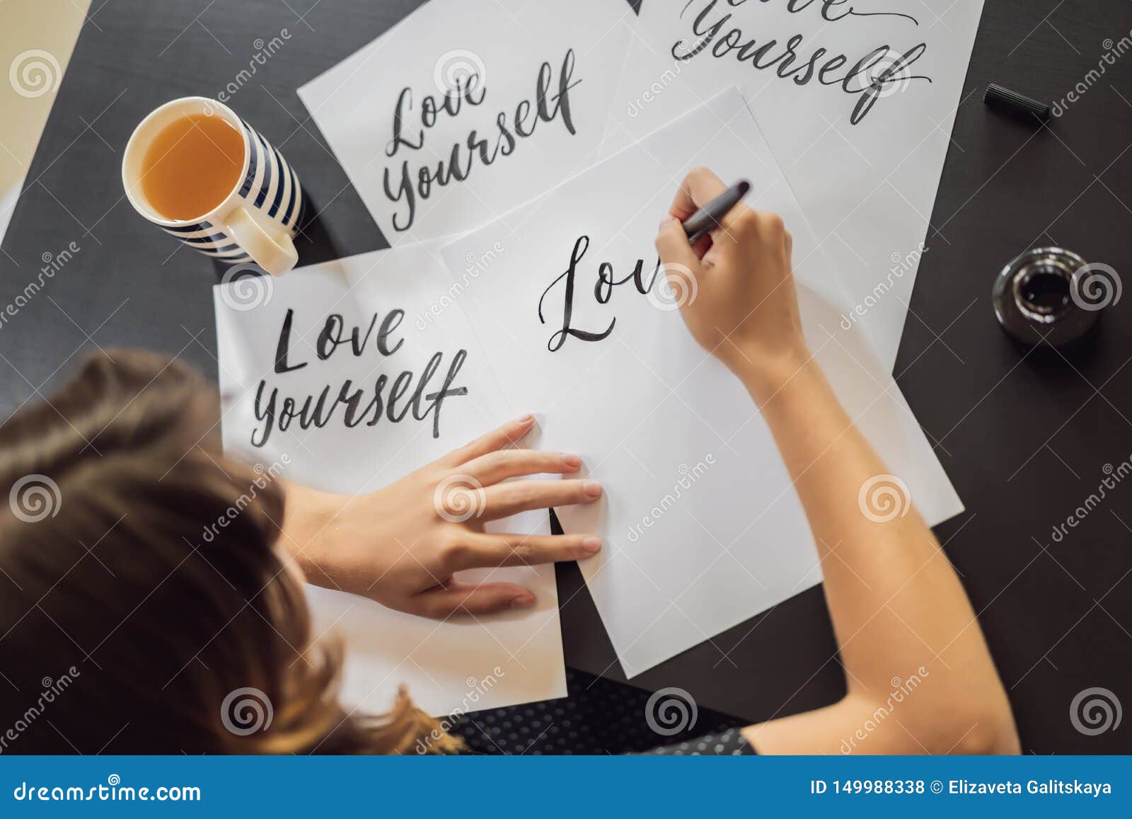 Love yourself. Calligrapher Young Woman writes phrase on white paper. Inscribing ornamental decorated letters. Calligraphy, graphic design, lettering, handwriting, creation concept.