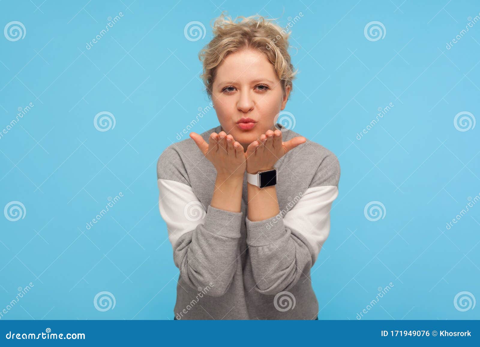 lovely sensual woman with short curly hair in casual sweatshirt sending air kiss to camera, expressing affection and fondness