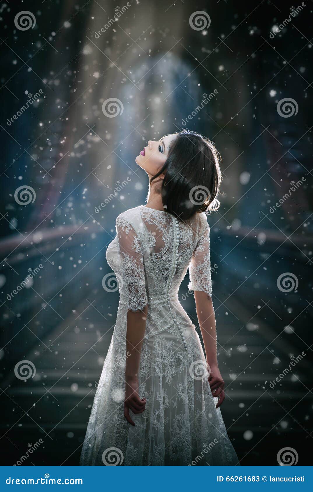lovely young lady wearing elegant white dress enjoying the beams of celestial light and snowflakes falling on her face